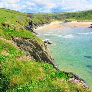 A coastal landscape with a sandy beach, grassy cliffs, and clear blue waters. - Dog Friendly Holiday Home in Newquay Cornwall (St. Columb Major)