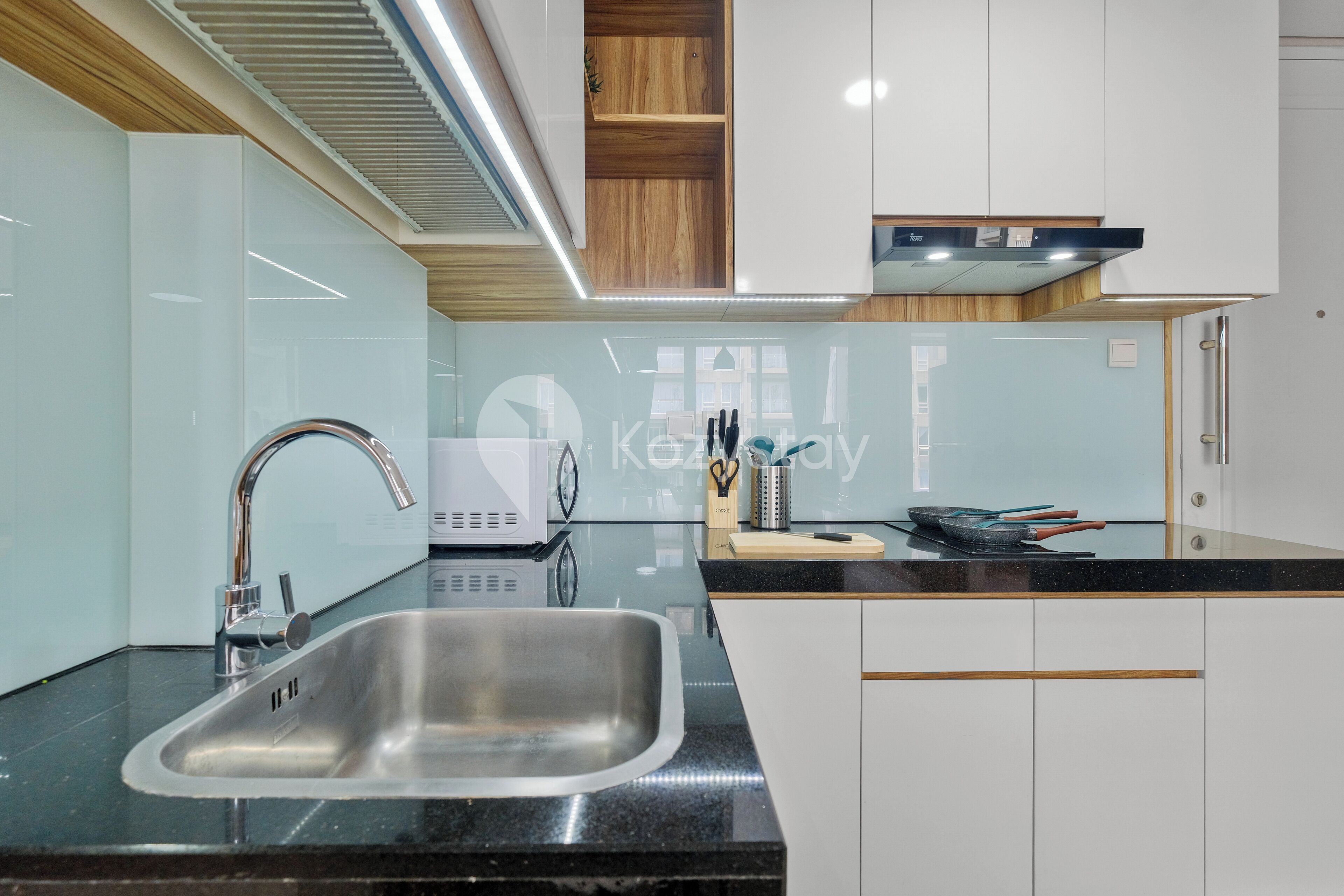 Een moderne keuken met een roestvrijstalen spoelbak, zwarte aanrechtbladen en witte keukenkastjes.