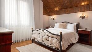 Een slaapkamer met een houten plafond, een bed met een witte dekbedovertrek, twee nachtkastjes en een bijzettafeltje.