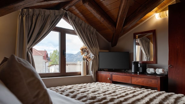 A bedroom with a bed, a TV, a dresser, and a window with curtains.