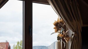 A bedroom with a large window, a bed, and a vase with flowers.