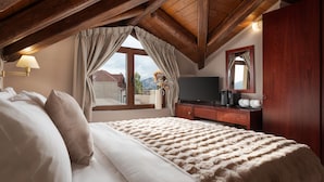 A bedroom with a large bed, wooden ceiling beams, a TV, and a window with curtains.