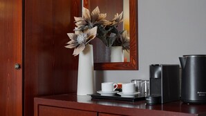 Une coiffeuse en bois avec un miroir, un vase blanc contenant des fleurs séchées, une machine à café et un réfrigérateur.