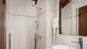 Une salle de bain avec une douche à parois de verre, un lavabo blanc et un sèche-cheveux fixé au mur.