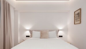 Una cama bien hecha con edredón blanco, dos almohadas y cabecera con luces empotradas.