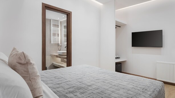 Un dormitorio moderno con una cama grande, un espejo, un televisor montado en la pared y un vestidor.