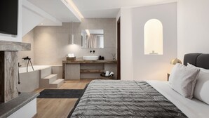Un dormitorio moderno con una cama grande, televisor empotrado, baño con lavamanos y espejo, y una escalera que sube a un nivel superior.
