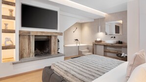 Un dormitorio moderno con chimenea, televisor grande, cama con manta de piel y baño con espejo grande y lavamanos.