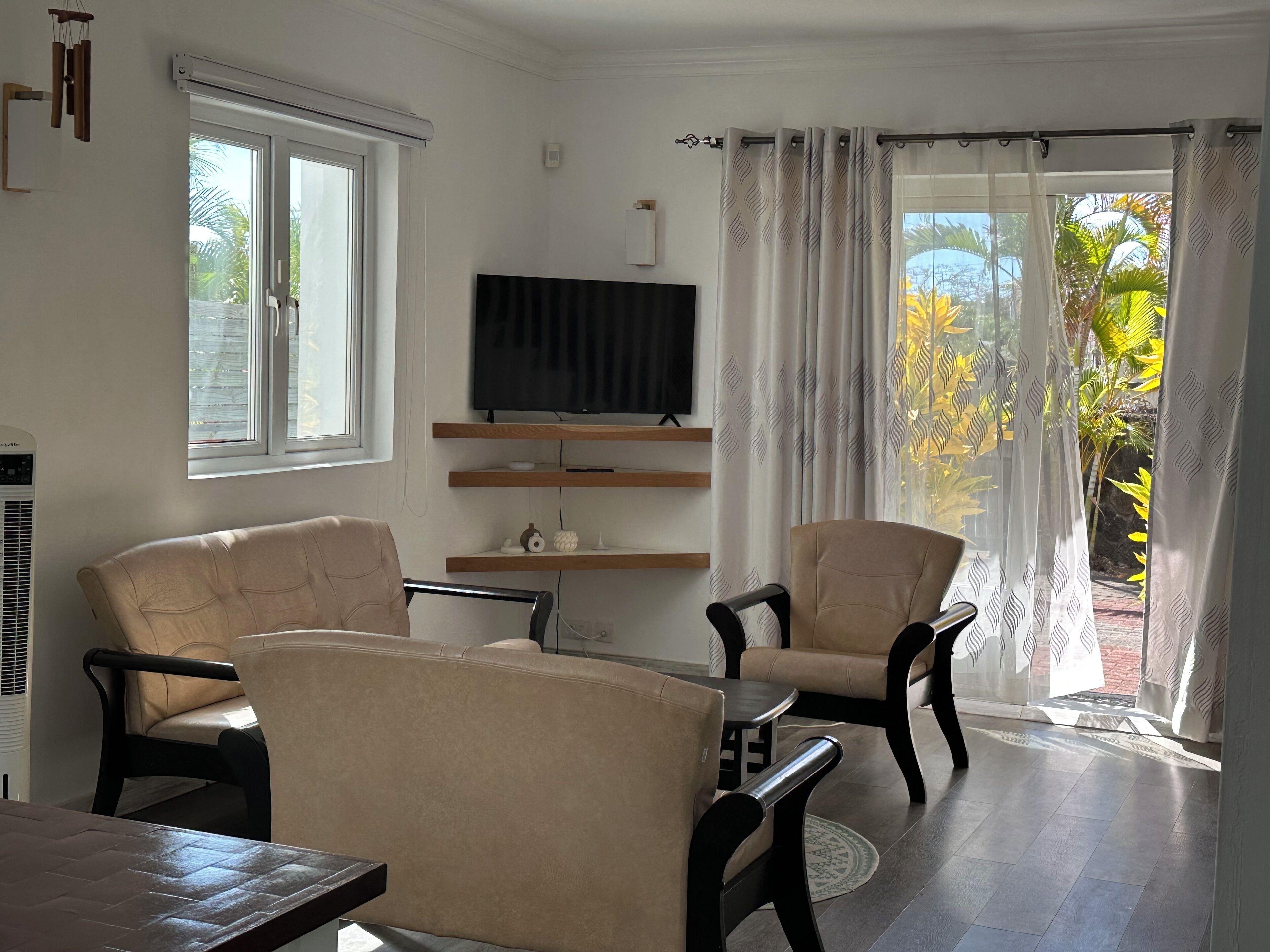 A living room with two beige armchairs, a wooden coffee table, and a flat-screen TV on a wooden shelf.