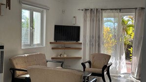 A living room with two beige armchairs, a wooden coffee table, and a flat-screen TV on a wooden shelf. - Charming 3 bed villa 10 mins to the nearest & most beautiful beach in Mauritius (Morcellement Swan, Pereybere, Grand Baie)
