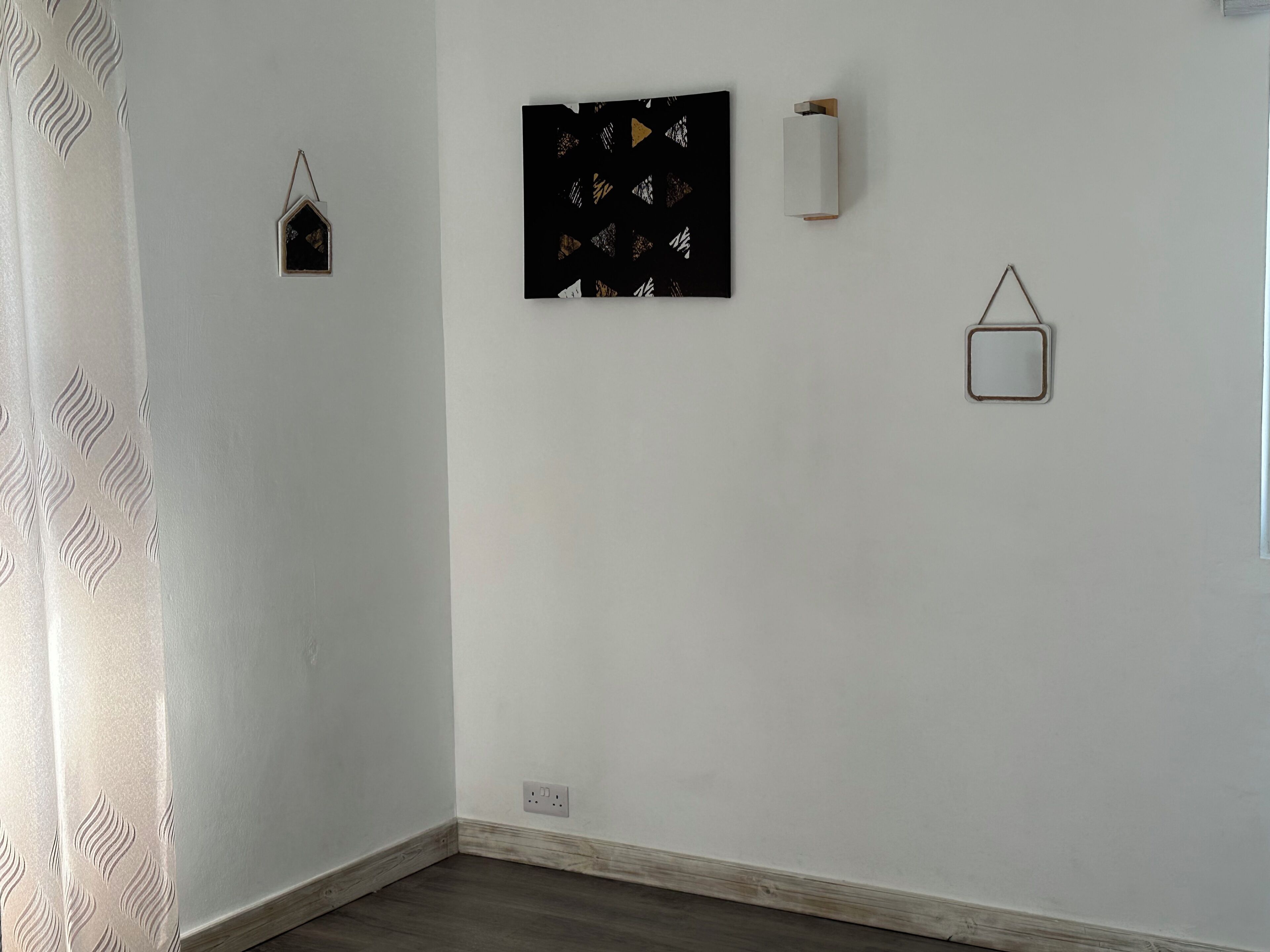 A room with a white wall, a black artwork, a small white light, and a metal square frame.