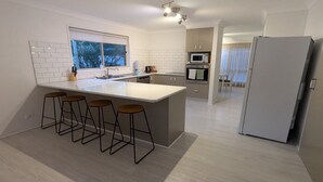 Una cocina moderna con una isla central, taburetes de bar, microondas, horno y refrigerador.