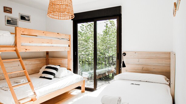 Une chambre avec deux lits superposés en bois, un lit simple et une grande fenêtre donnant sur un paysage verdoyant.