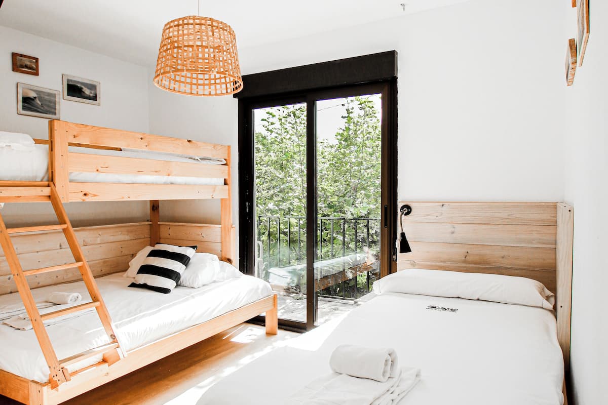 Een slaapkamer met twee houten stapelbedden, een enkel bed en een groot raam met uitzicht op groen.