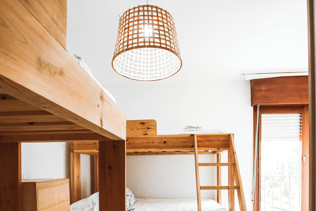 Een slaapkamer met een houten stapelbed, een trapje, een houten bureau en een hanglamp.