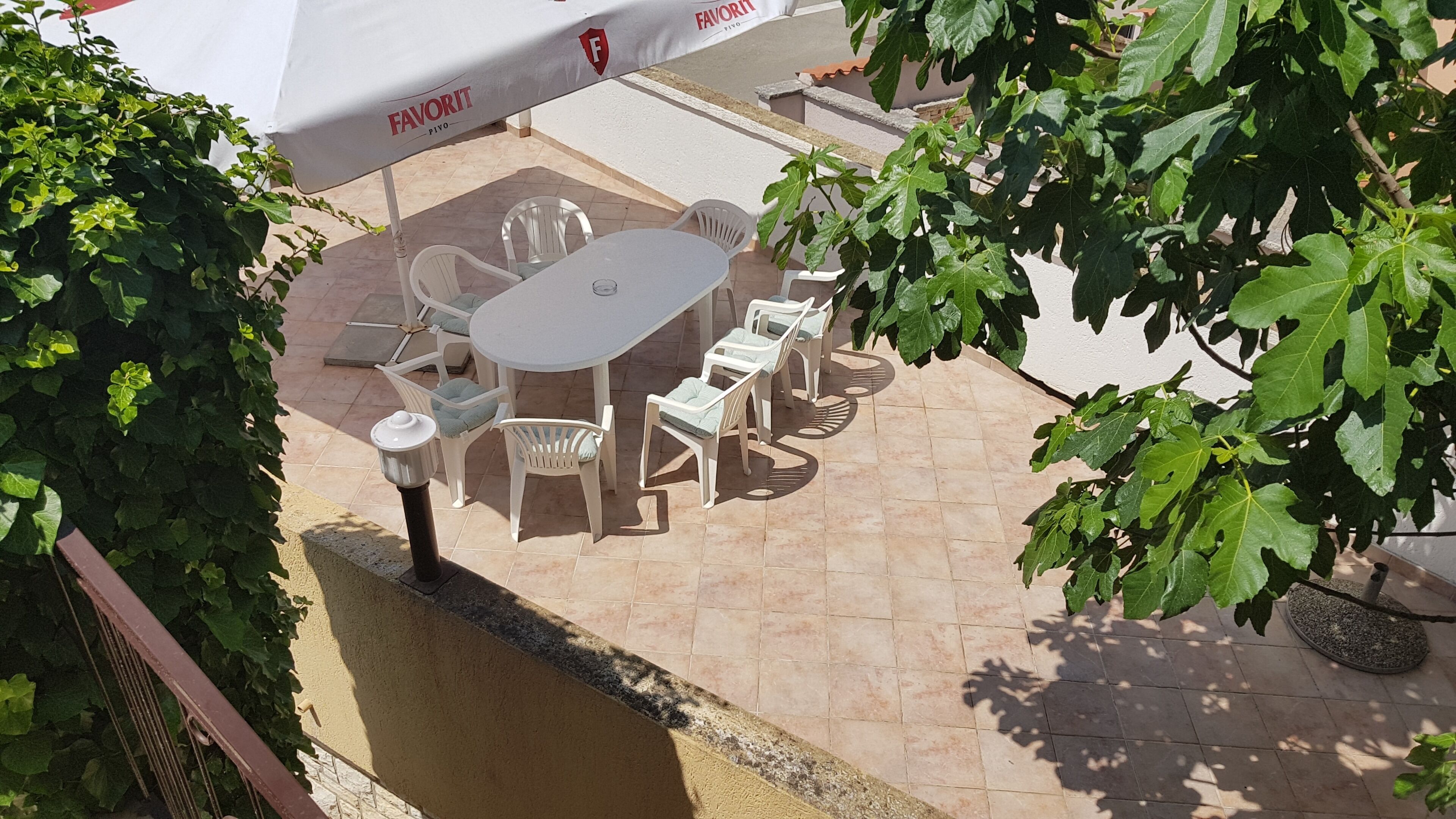 An outdoor patio with a round table and chairs, a white umbrella, and greenery.