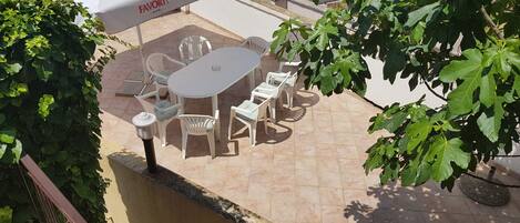 An outdoor patio with a round table and chairs, a white umbrella, and greenery.