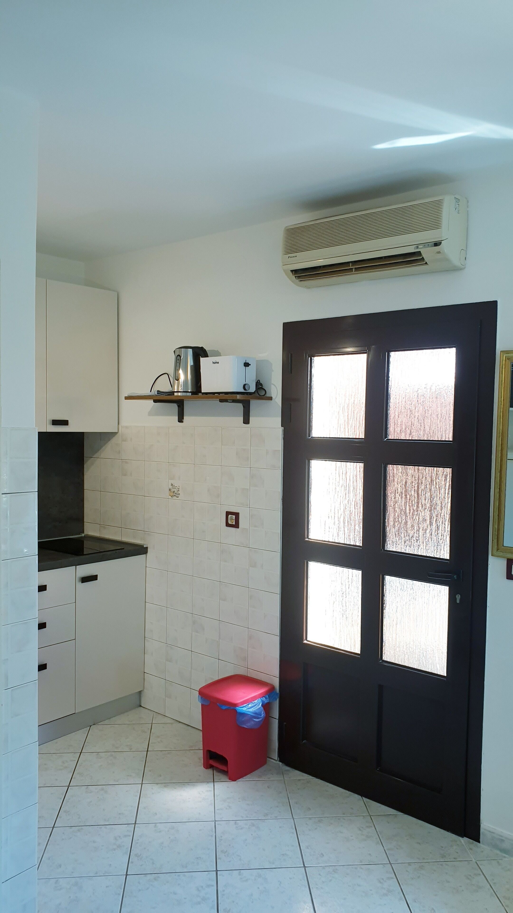 A small kitchen with white cabinets, a black countertop, a red stool, and a black door with glass panels.