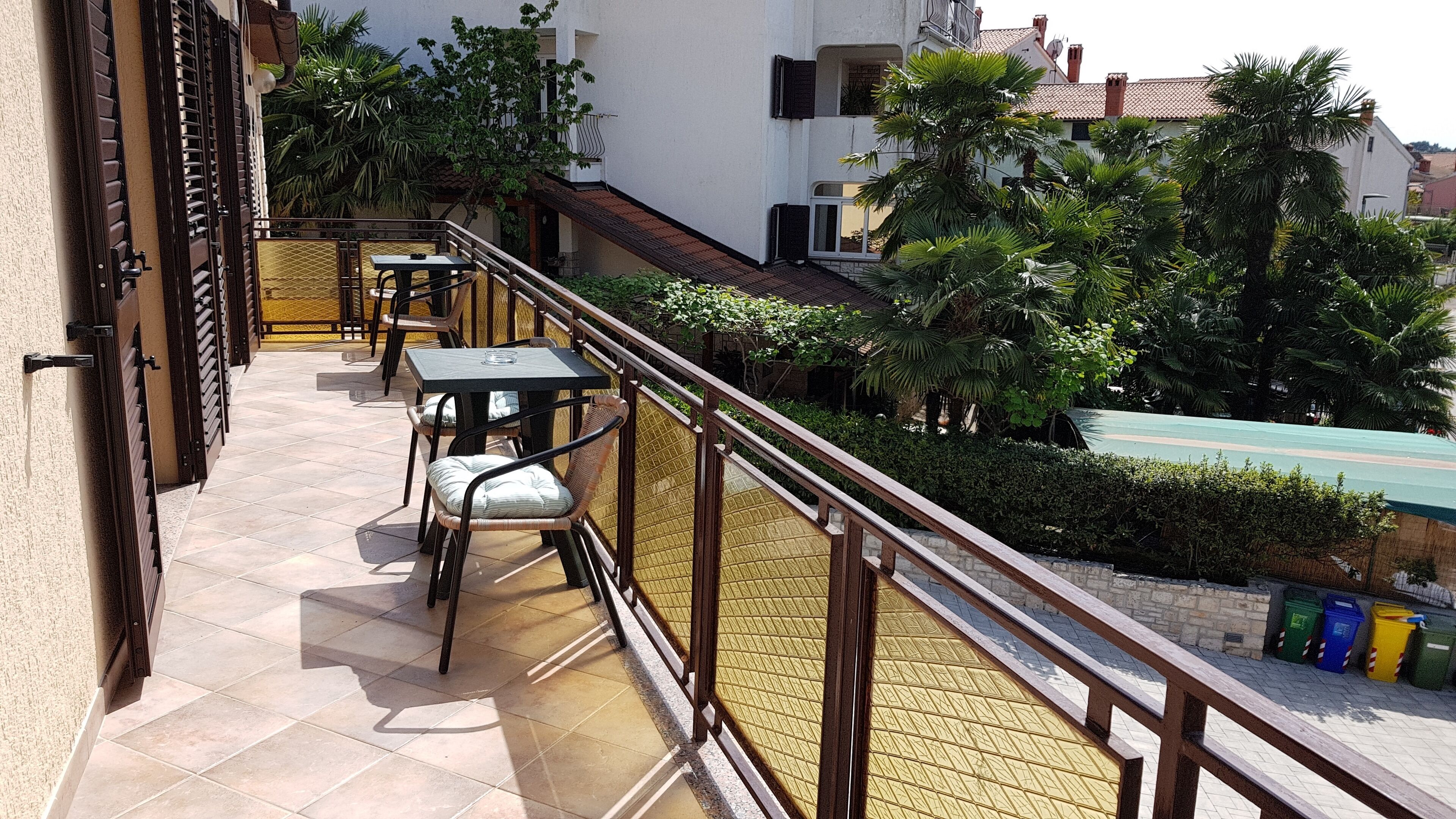 Un balcón con mobiliario exterior, vistas de los edificios circundantes y una piscina verde al fondo.