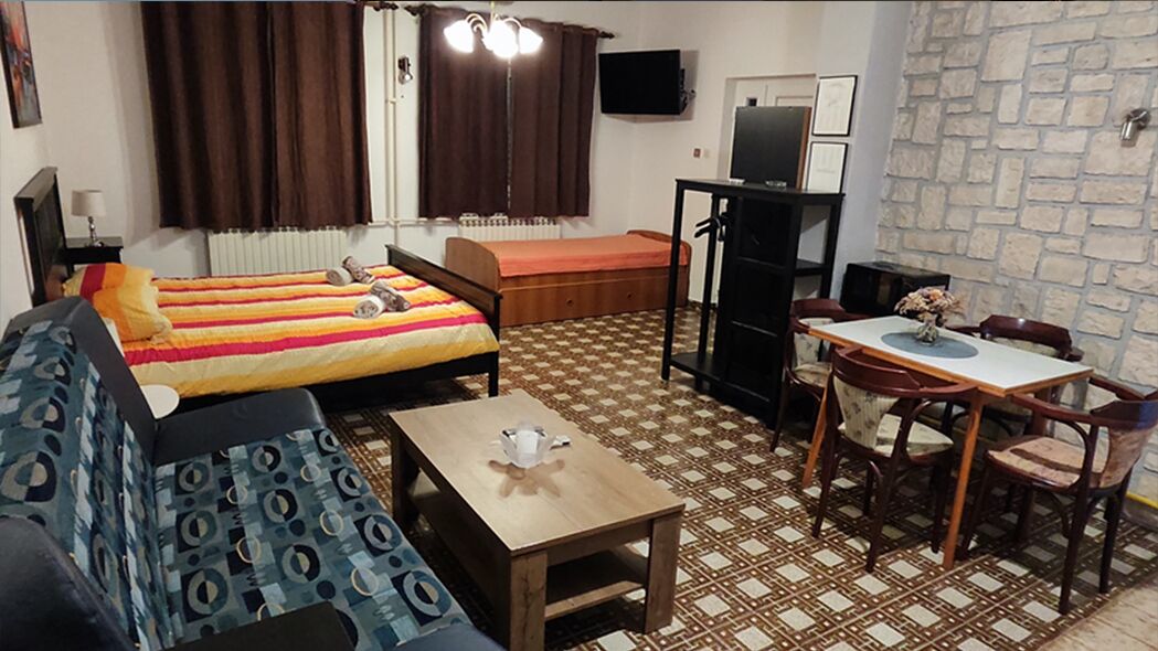 A small, furnished room with a bed, a sofa, a table, and a desk.