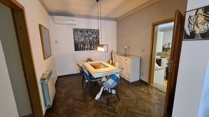A compact kitchen with a dining area, featuring a herringbone wood floor, a white cabinet, and a hanging pendant light. - Pablo accommodation (Rovinj)