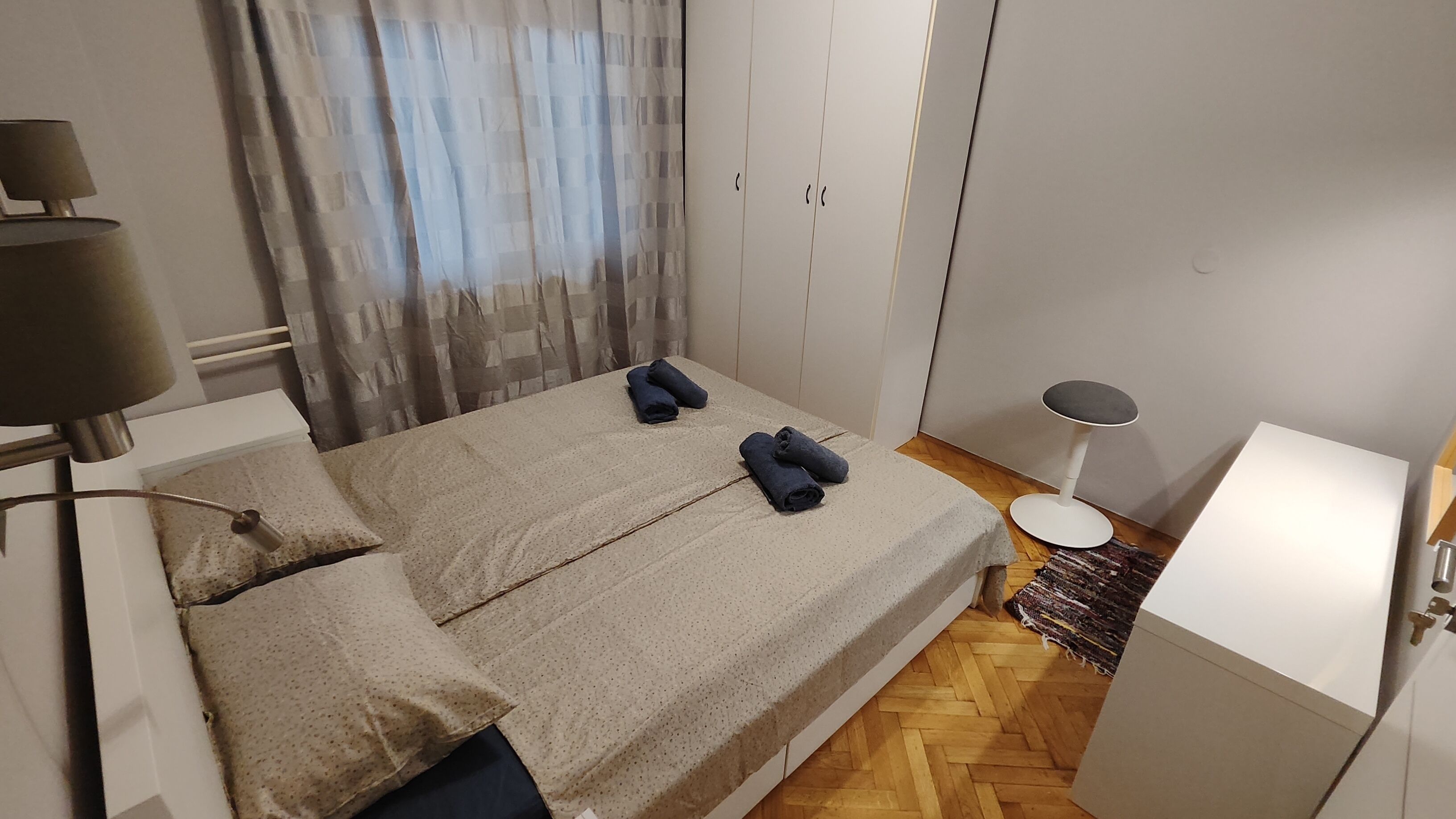 A bedroom with a bed, a lamp, a wardrobe, and a small table.