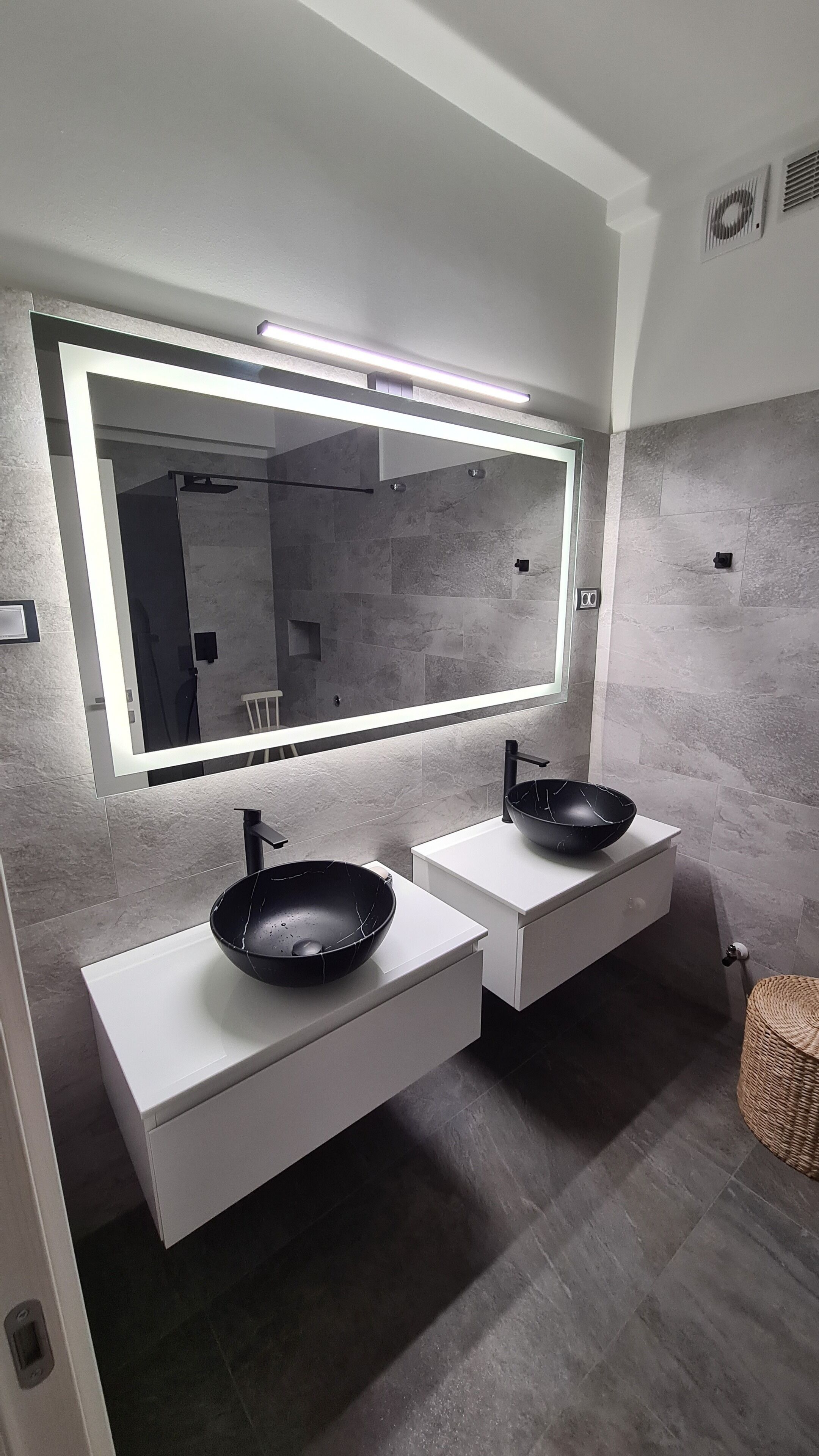 A modern bathroom with two sinks, a large mirror, and a wall-mounted light.
