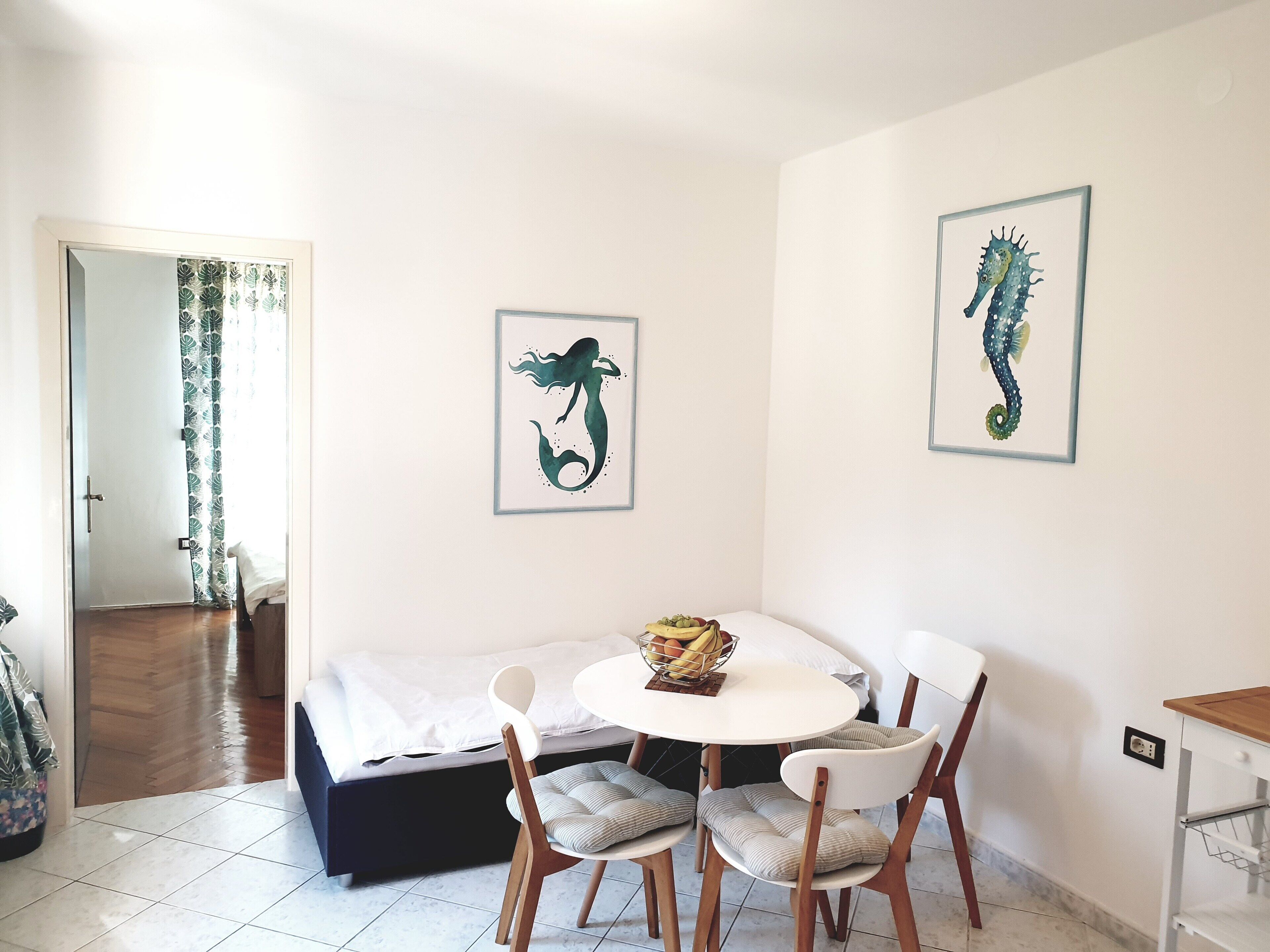 Een kamer met een bed, een ronde tafel met stoelen en twee kunstwerken van zeepaardjes in een lijst aan de muur.