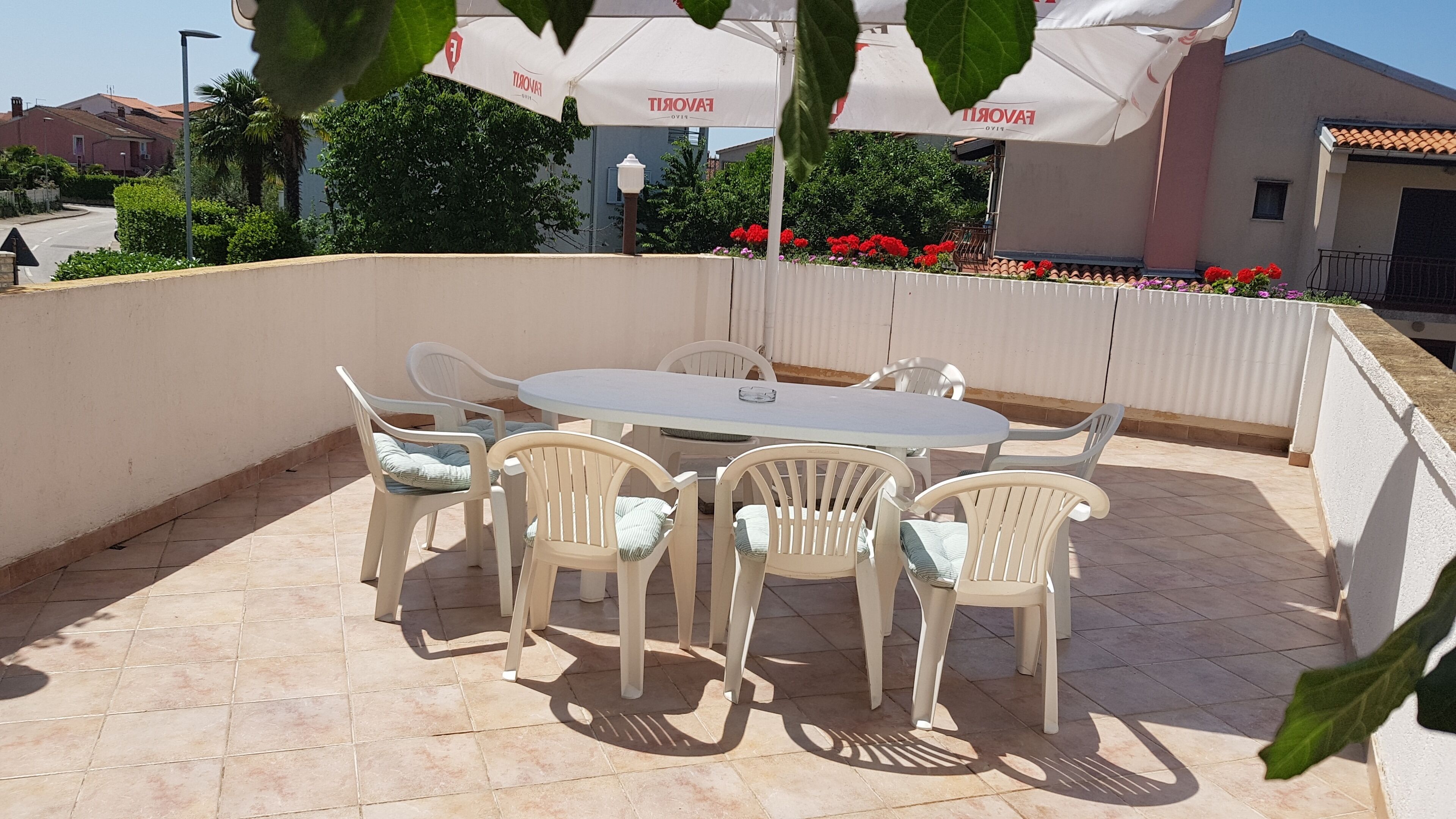 An outdoor patio with a round table and six chairs, surrounded by a white wall and a tiled floor.