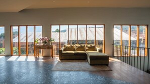 A spacious living room with a sectional sofa, a coffee table, and a view of a traditional building through large windows. - Noya Hotel (Kintamani)