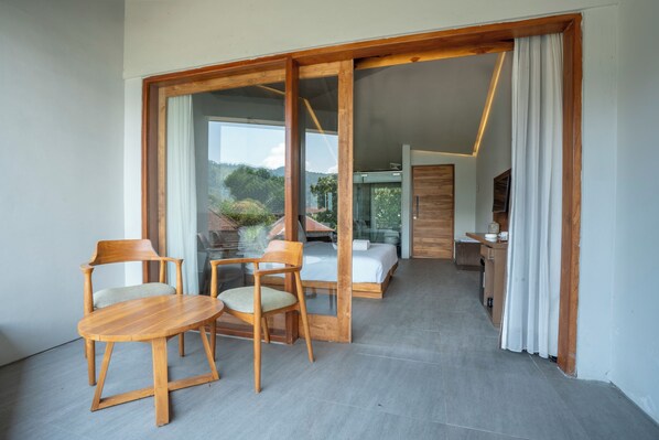 A modern hotel room with a wooden dining set, a bed, and a view of the outdoors. - Noya Hotel (Kintamani)