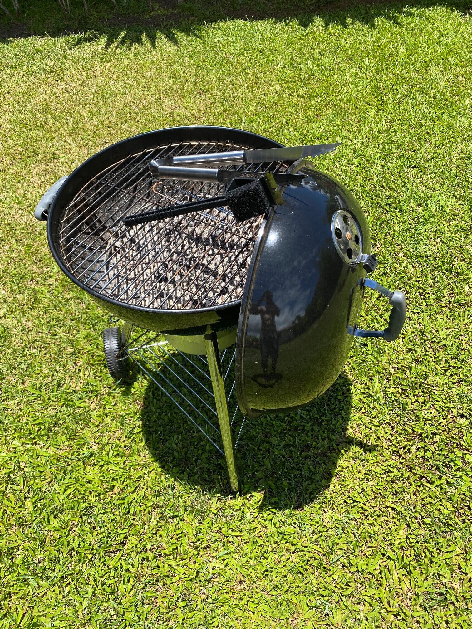Un barbecue portatif à charbon de bois, doté d’un couvercle et de poignées, posé sur une pelouse.