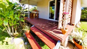 A wooden deck with a table and chairs, surrounded by potted plants and a glass door leading to a covered area.