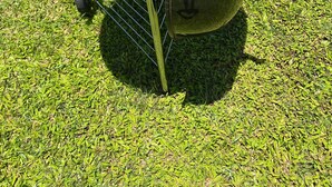 A portable charcoal grill with a lid and handles, placed on a grassy lawn.