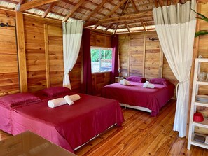 A wooden cabin room with two beds, a small table, and a shelf with glasses. - RAIATEA - Orion Pool Bungalow (Uturoa)