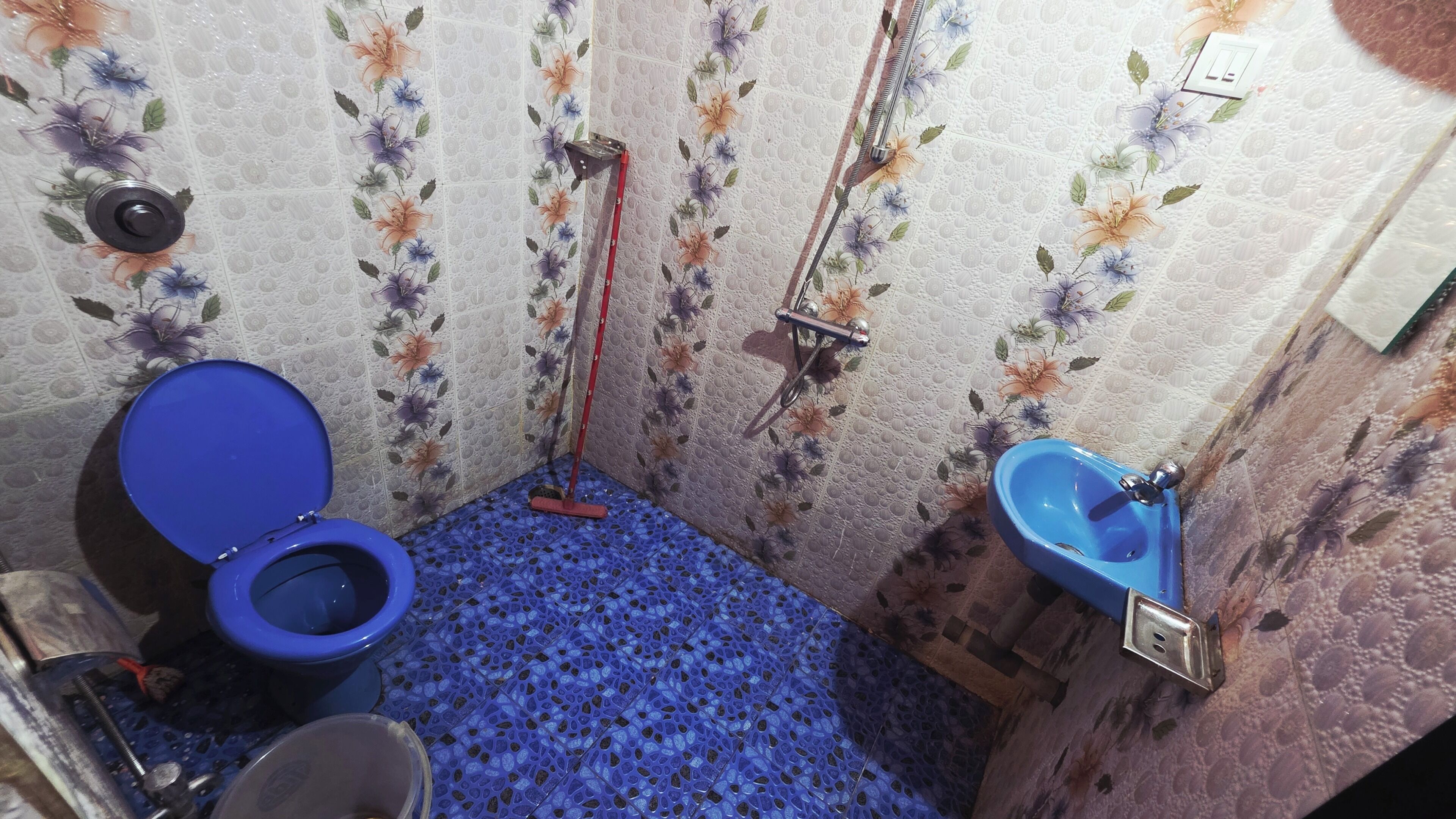 Un baño con inodoro y lavamanos azules, y una ducha con manguera roja.