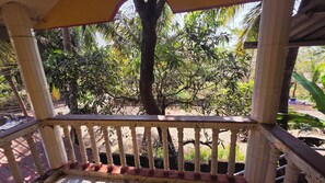 A covered outdoor area with a wooden railing, surrounded by trees and vegetation. - Vailankani guest house (Canacona)
