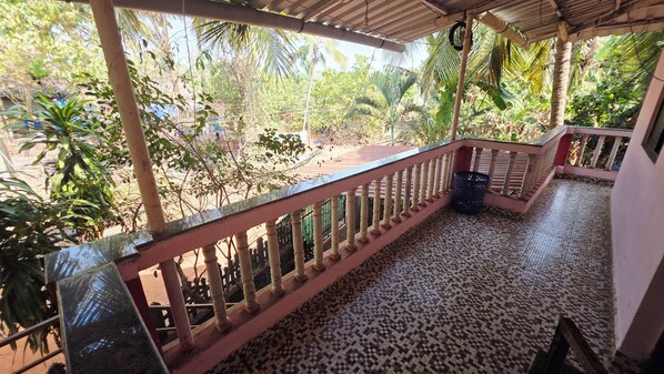 Un balcon fermé doté d’un sol carrelé, d’une rambarde en métal et offrant une vue sur un jardin où poussent diverses plantes et arbres.