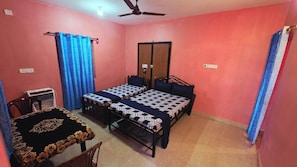 Una habitación con dos camas, una mesa, una silla, un ventilador de techo y una puerta.