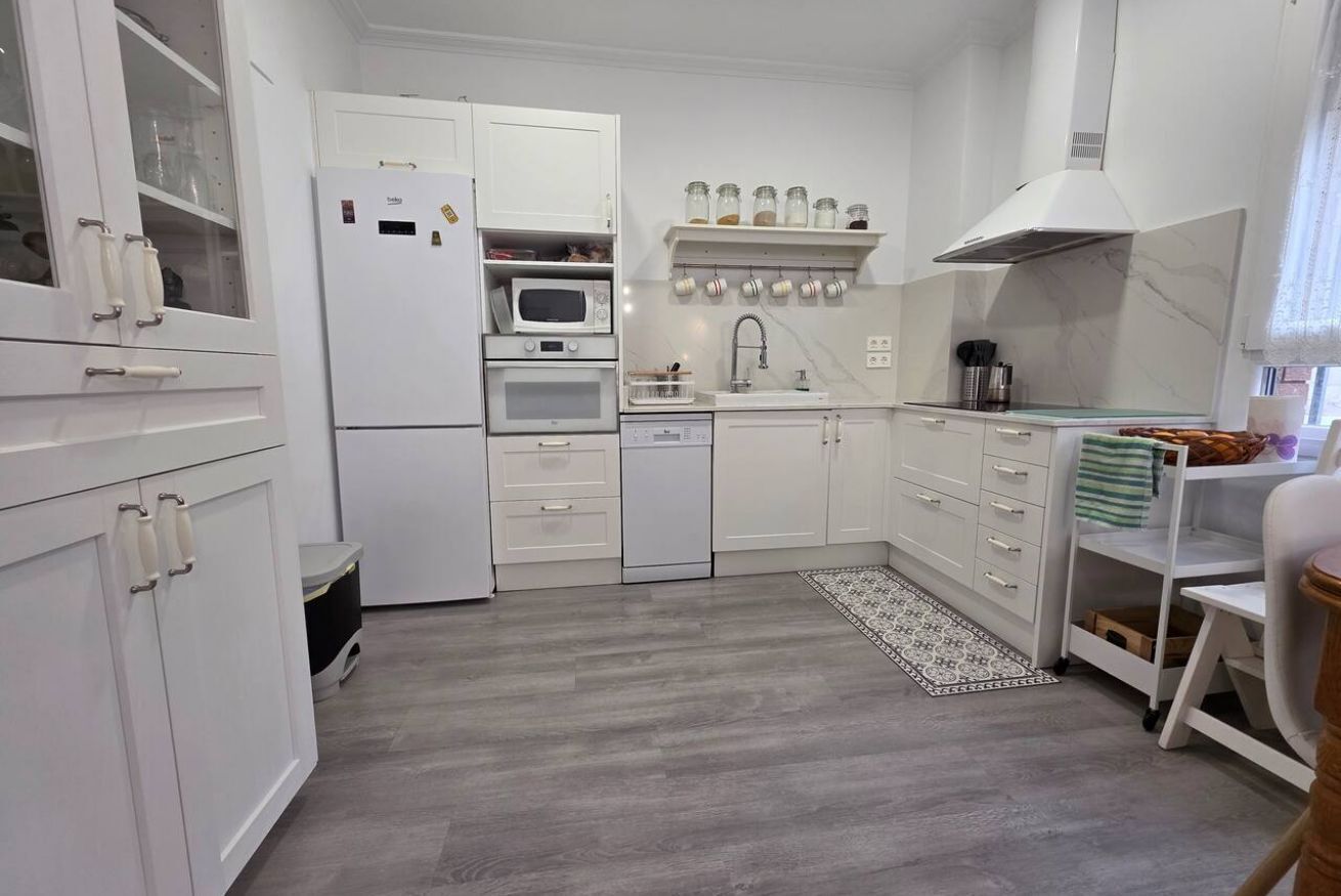 Cocina compacta con armarios blancos, microondas, horno, pileta y una mesada pequeña.