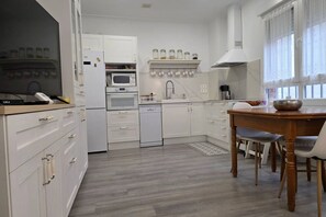 A modern kitchen with white cabinetry, a built-in oven, a microwave, a dishwasher, and a dining area with a wooden table and chairs.