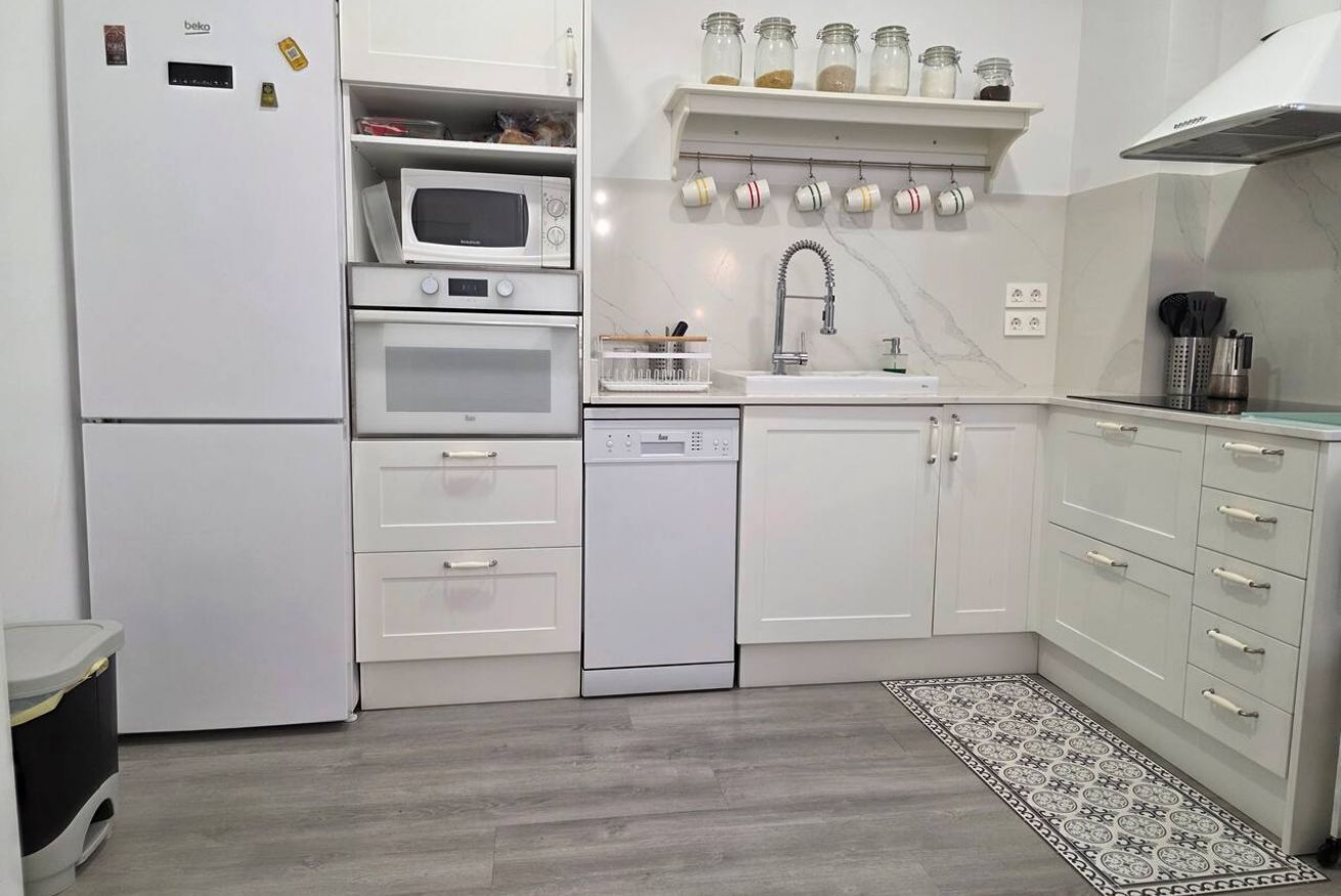 Una cocina con armarios blancos, microondas, horno, lavavajillas y fregadero.