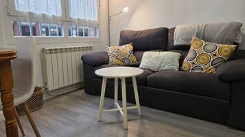 Una sala de estar con un sofá oscuro, una mesita blanca y cojines estampados.