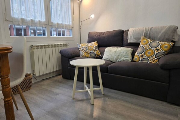 A living room with a dark sofa, a small white table, and patterned cushions.