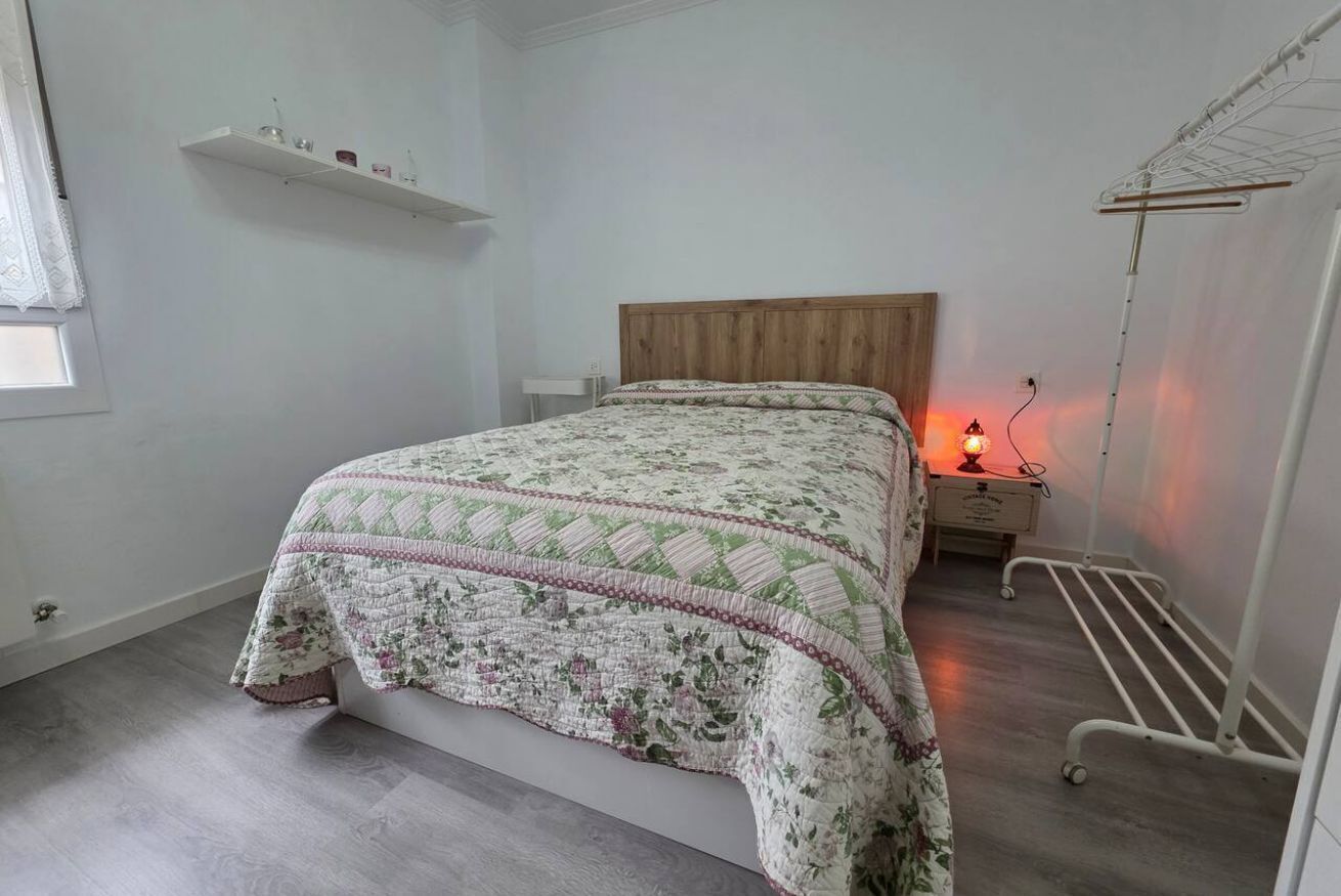 Un dormitorio con una cama, una mesita de noche con lámpara, una estantería y un radiador.