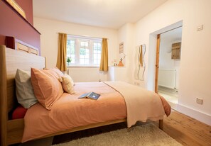 Um quarto com cama, janela com cortinas, radiador e espelho na parede.