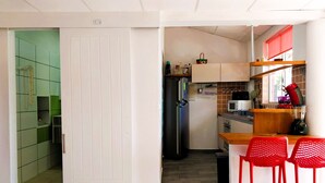 A compact kitchen with a refrigerator, microwave, and a small countertop. There are two red chairs and a window with a red blind. - TAHITI - Terevete Pool Studio (Arue)
