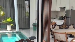 A bedroom with a bed, a view of a pool, and a kitchen area. - Serene Bali Villa With Private Pool and Antiqued Charm (Denpasar)
