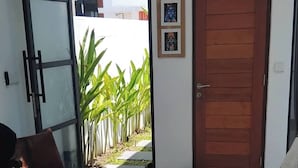 A modern living room with a glass door leading to a balcony, a wooden door, and a sofa with a unique design. - Serene Bali Villa With Private Pool and Antiqued Charm (Denpasar)