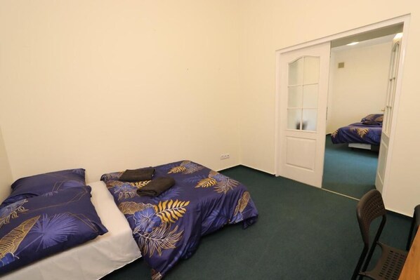 Een kleine kamer met twee bedden, een stoel en een deur naar een andere kamer.